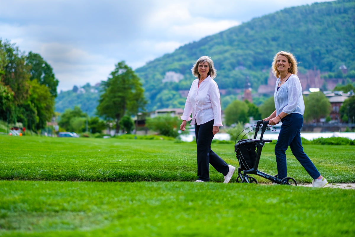 Zwei Frauen beim Spaziergang auf einer Wiese, eine mit dem Sunrise Gemino 30 Carbon Rollator