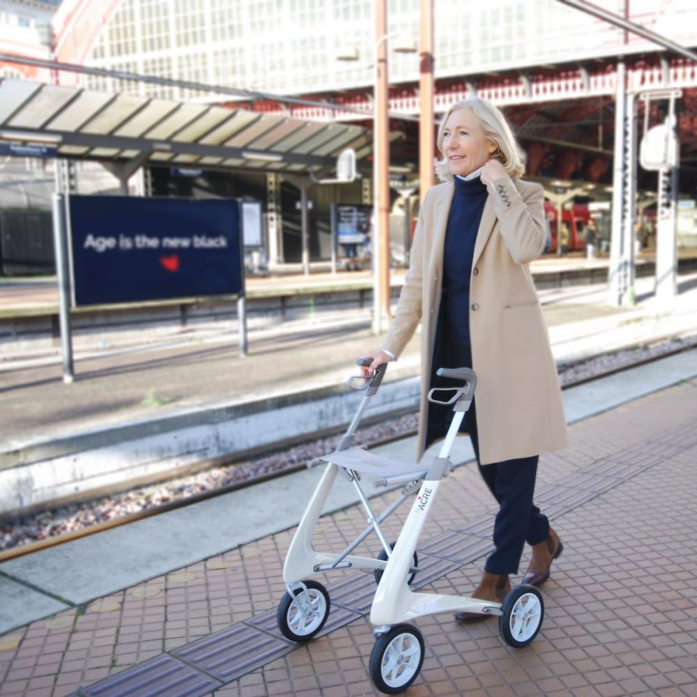 Frau geht mit einem weißen byACRE Carbon Ultralight Rollator über einen Bahnsteig